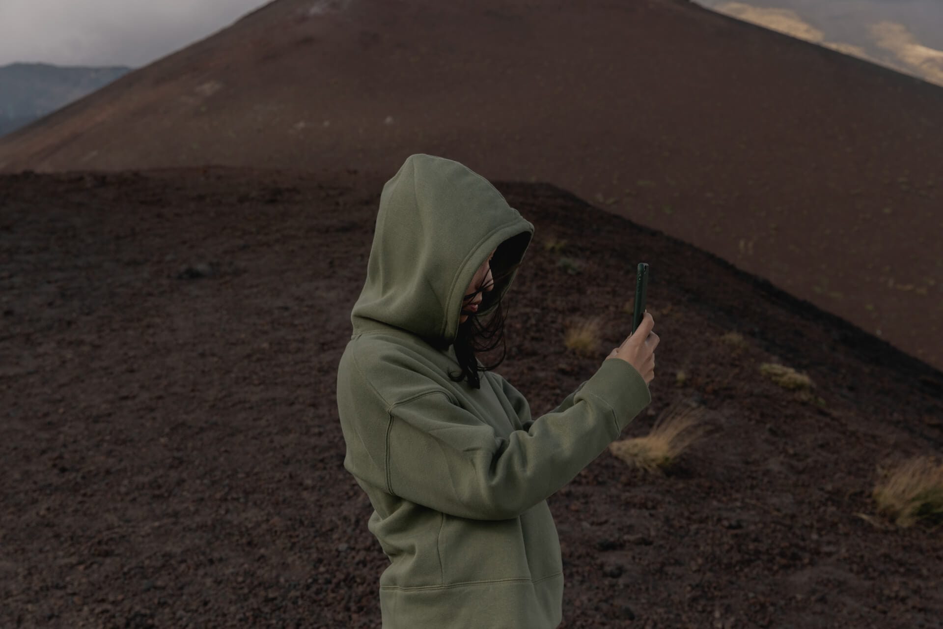 Person in hoodie taking photo on mountain.
