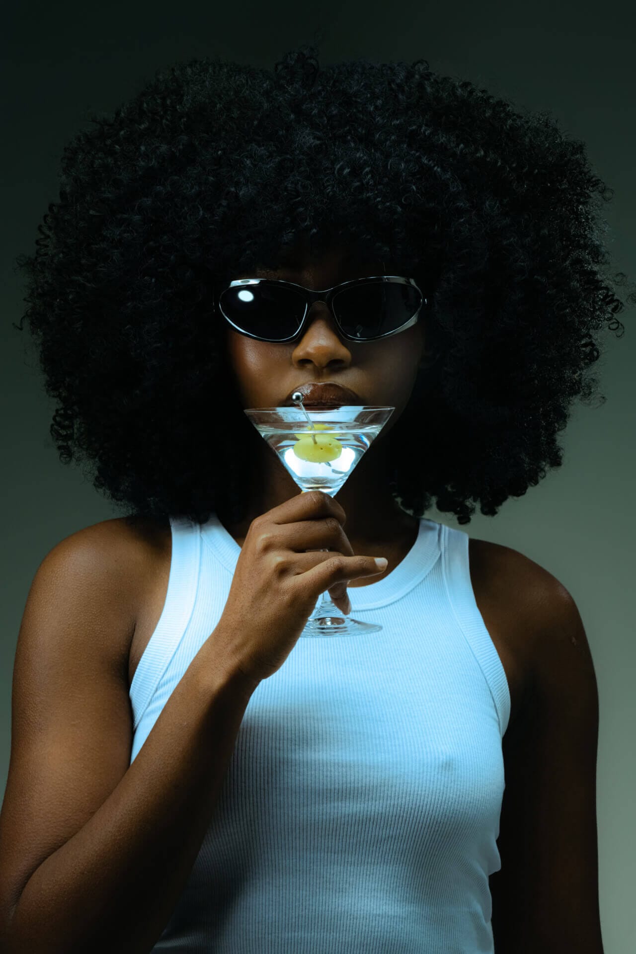 Woman with sunglasses holding a cocktail glass.