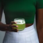 Person holding a green beverage in glass.