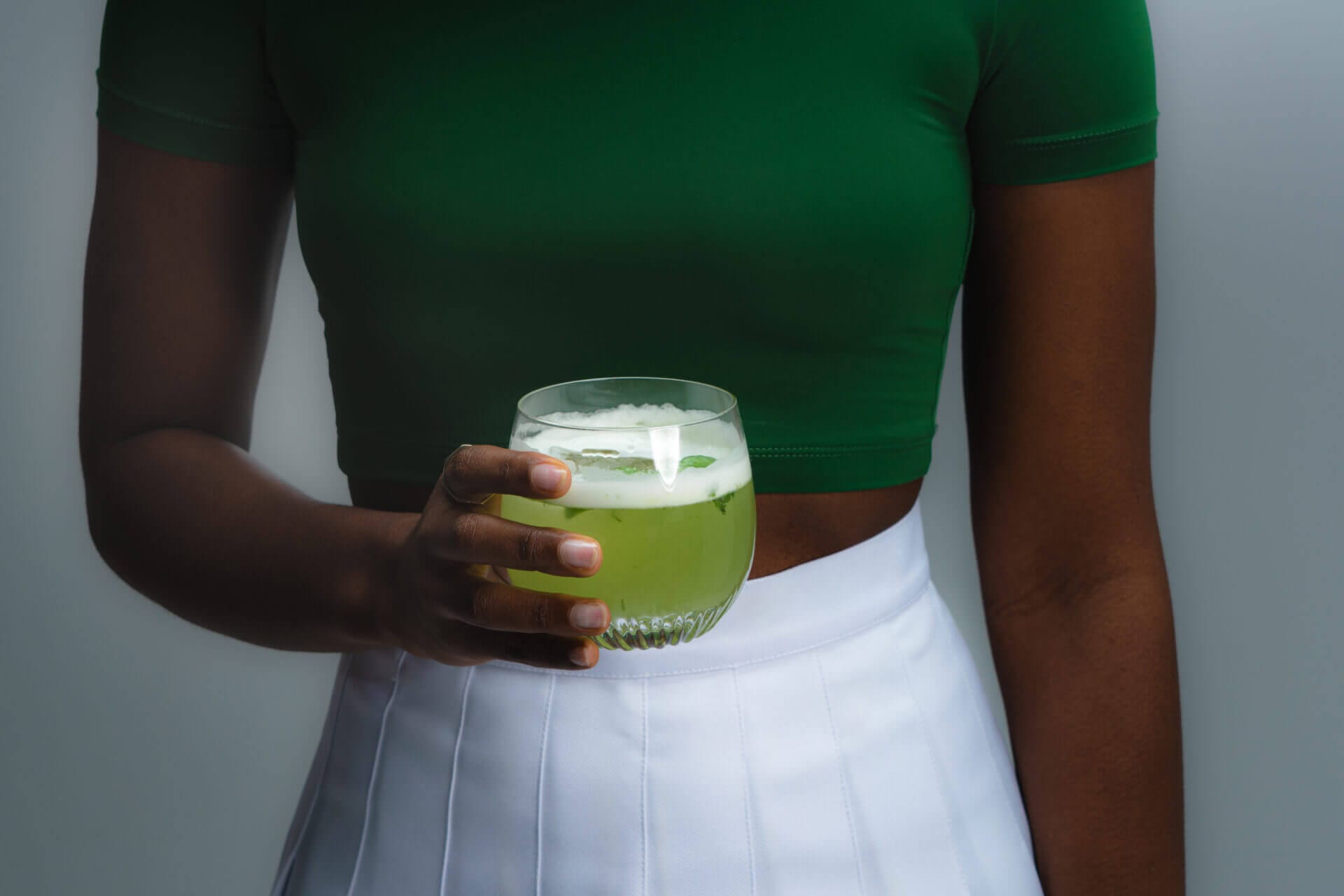 Person holding a green beverage in glass.