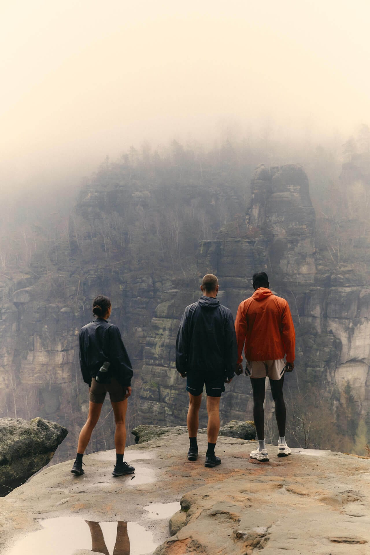 Three people standing on a misty cliff.