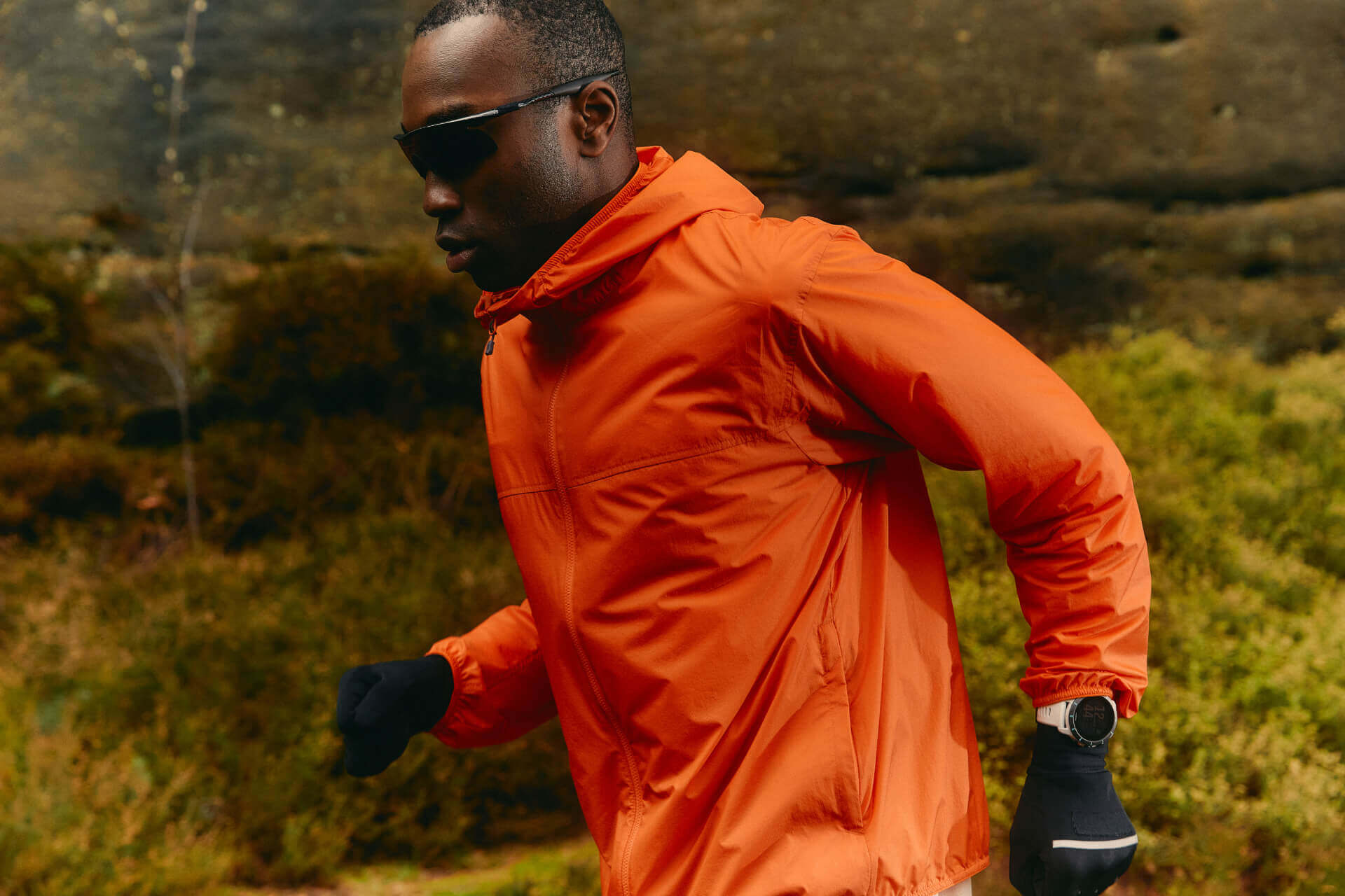 Man running outdoors in orange jacket.
