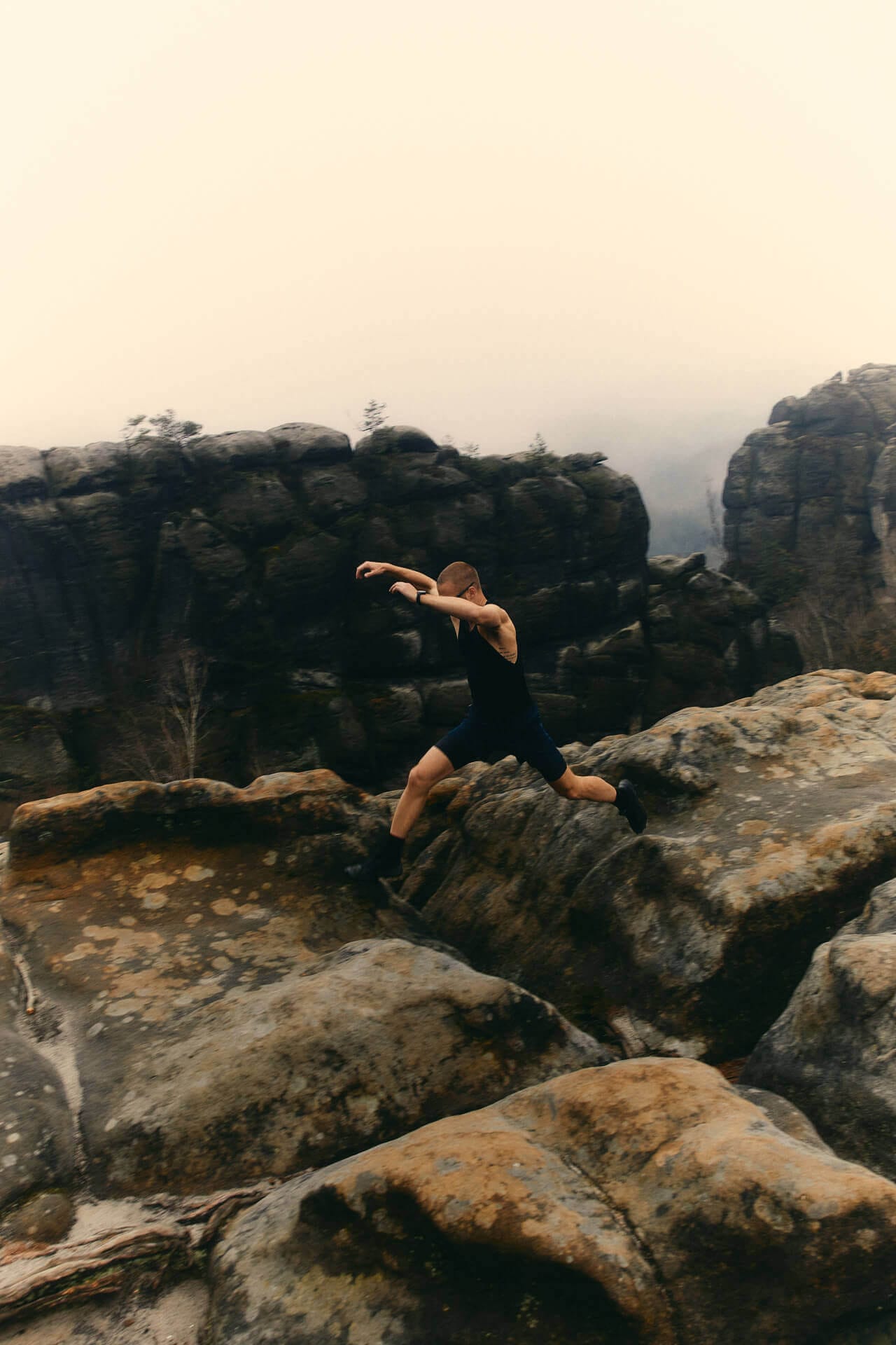 Person jumping on rocky landscape in fog.