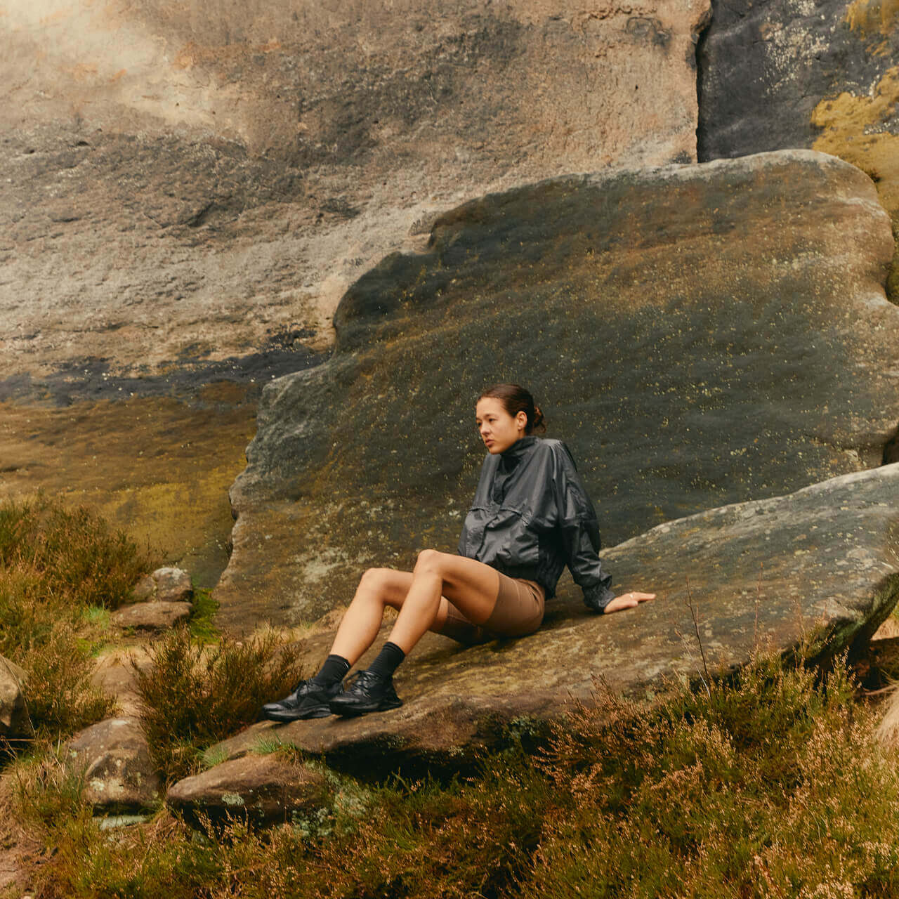 Person sitting on large rock outdoors.