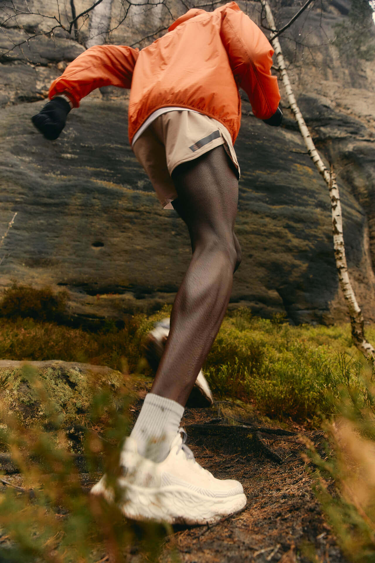 Runner in orange jacket climbing rocky path.