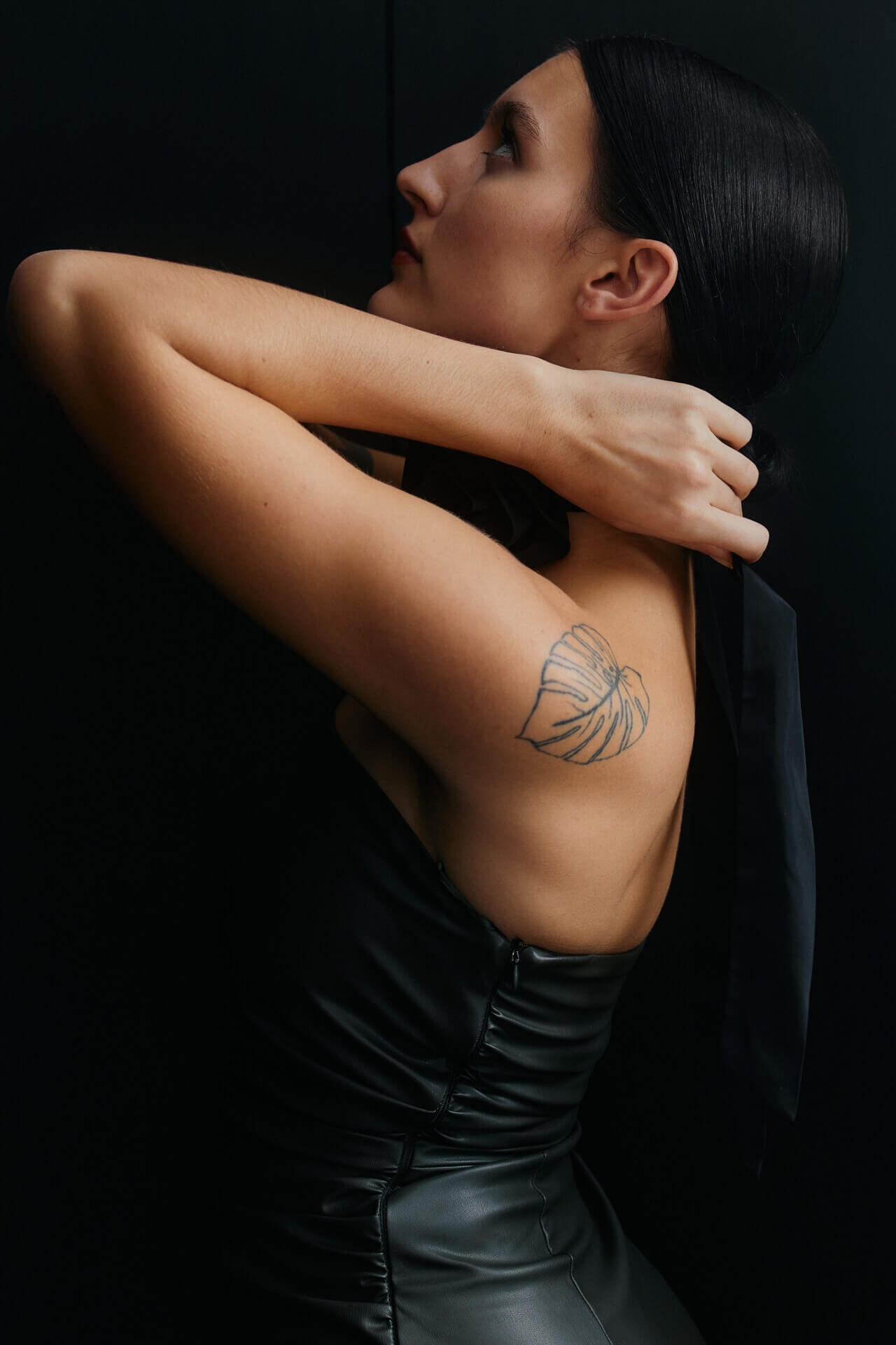 Woman with tattoo, adjusting black dress strap.