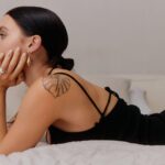 Woman lying on bed with shoulder tattoo.