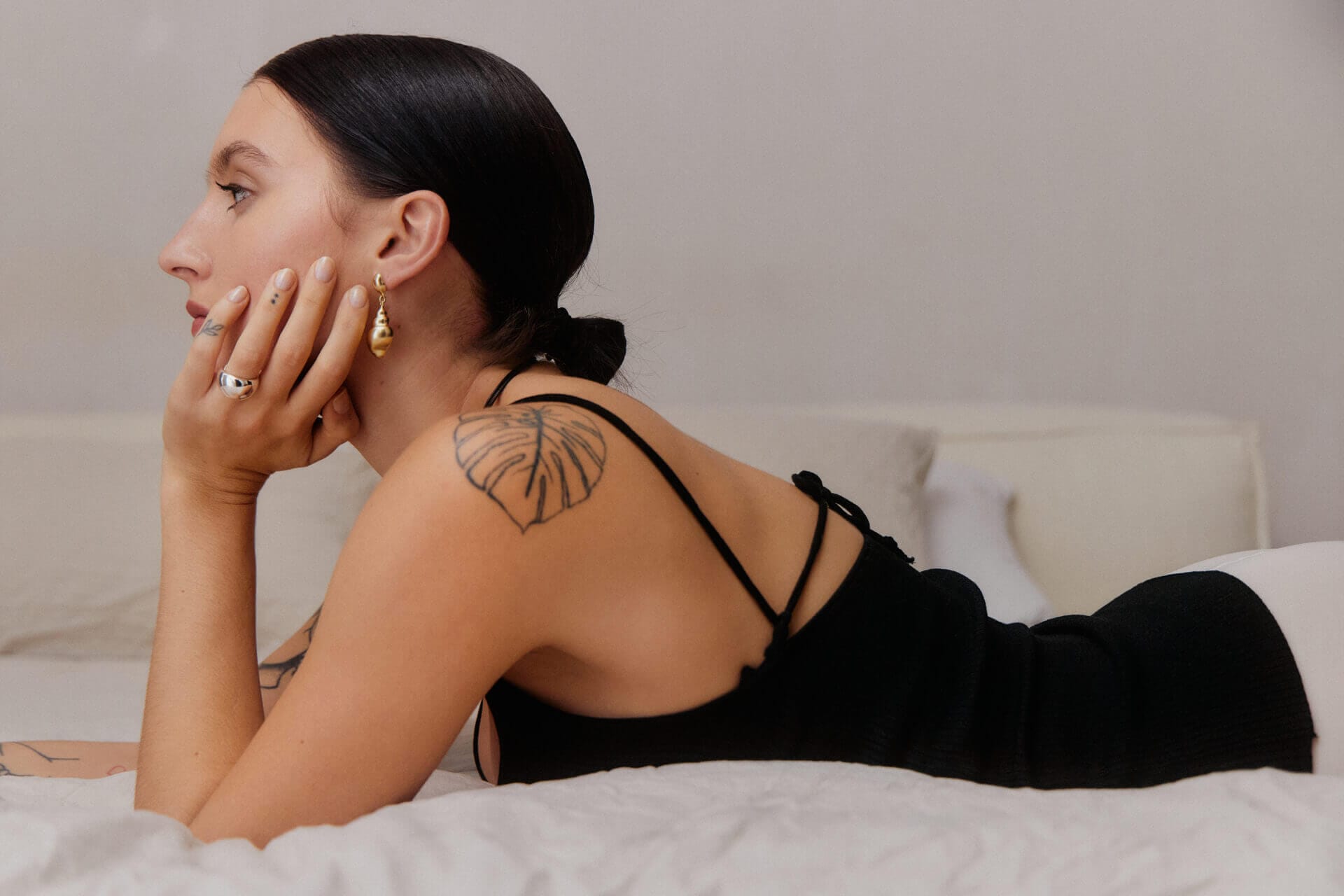 Woman lying on bed with shoulder tattoo.
