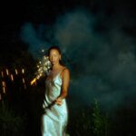 Woman holding sparkler in dark, smoky night.