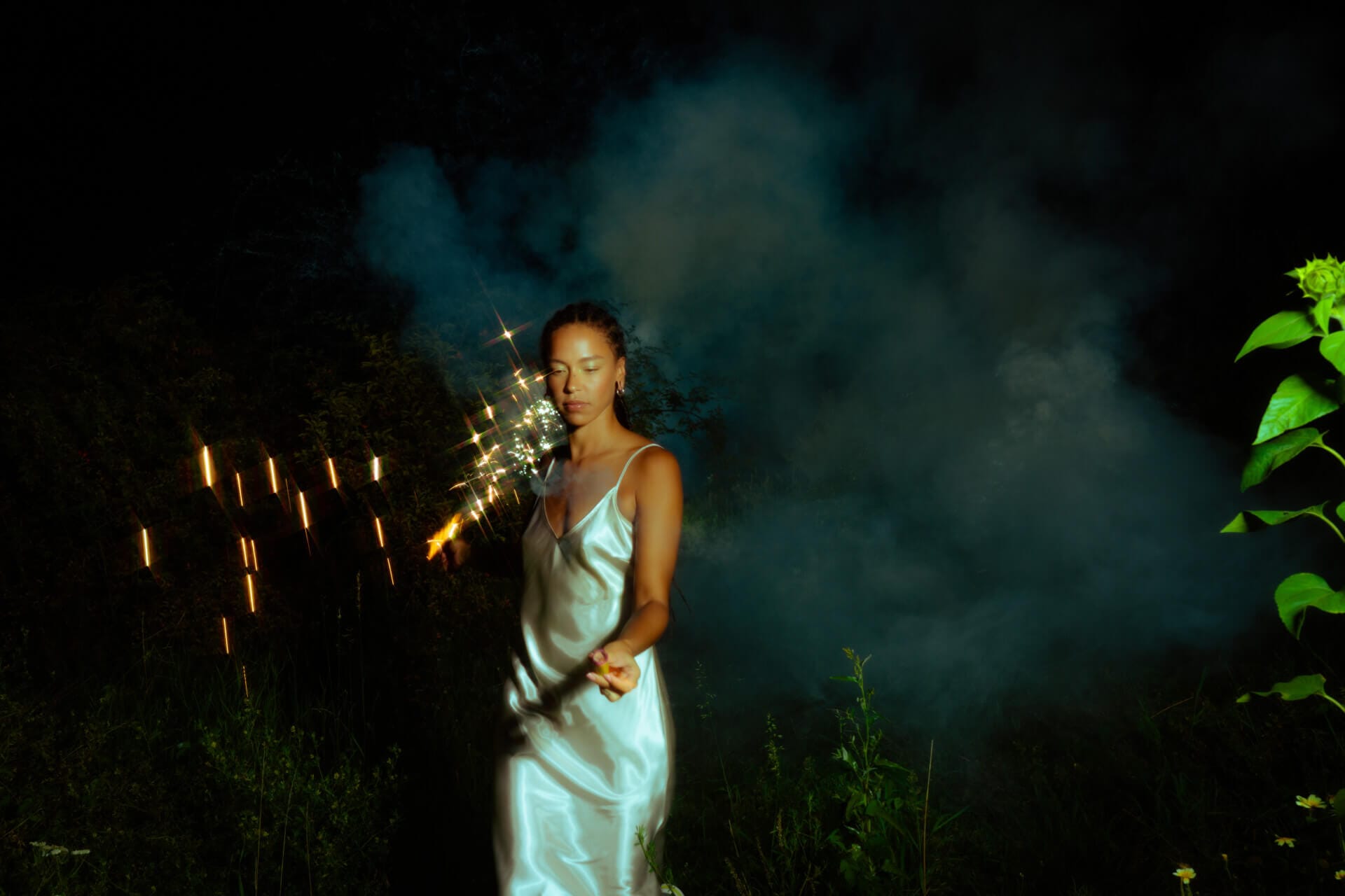 Woman holding sparkler in dark, smoky night.