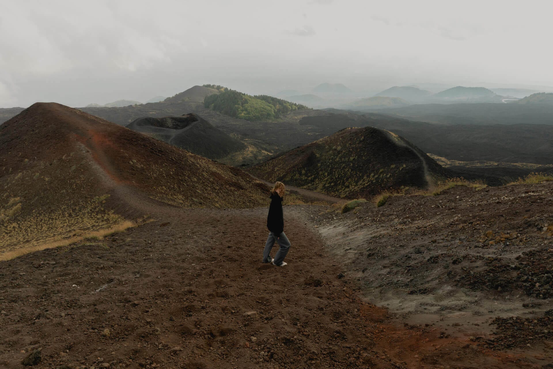 Person walking on volcanic landscape with hills.
