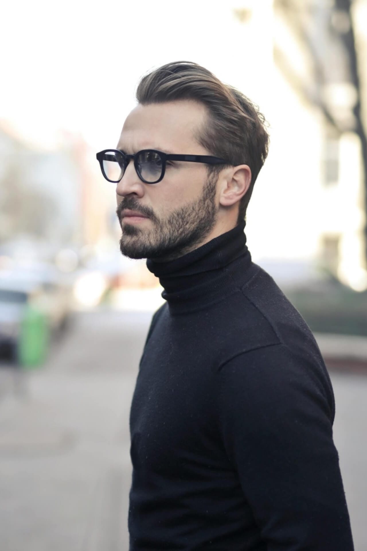 Man with glasses wearing black turtleneck outside.
