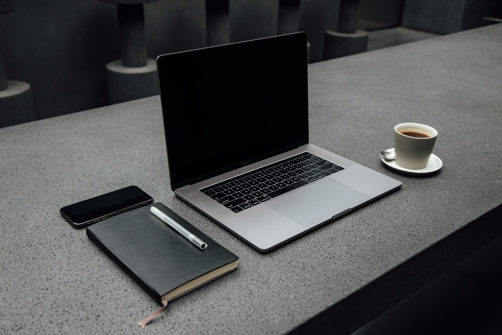 Laptop, notebook, phone, and coffee on table.