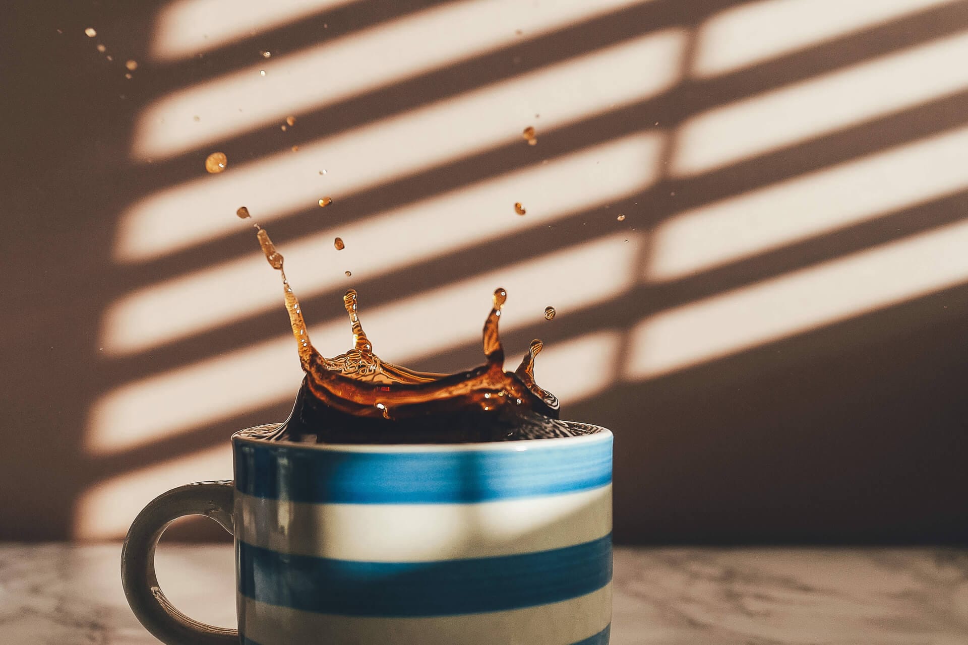 Coffee splash in striped mug, sunlight shadows.