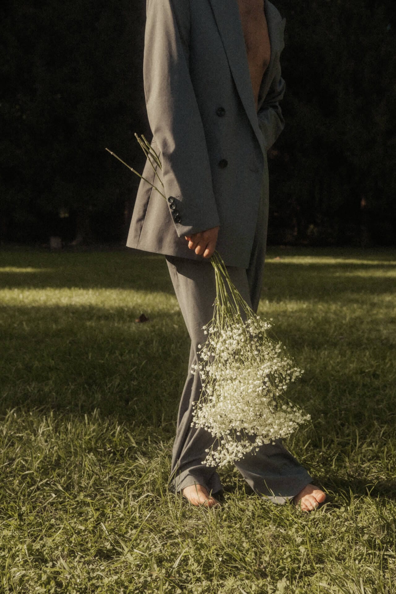 Person in suit holding white flowers outdoors.