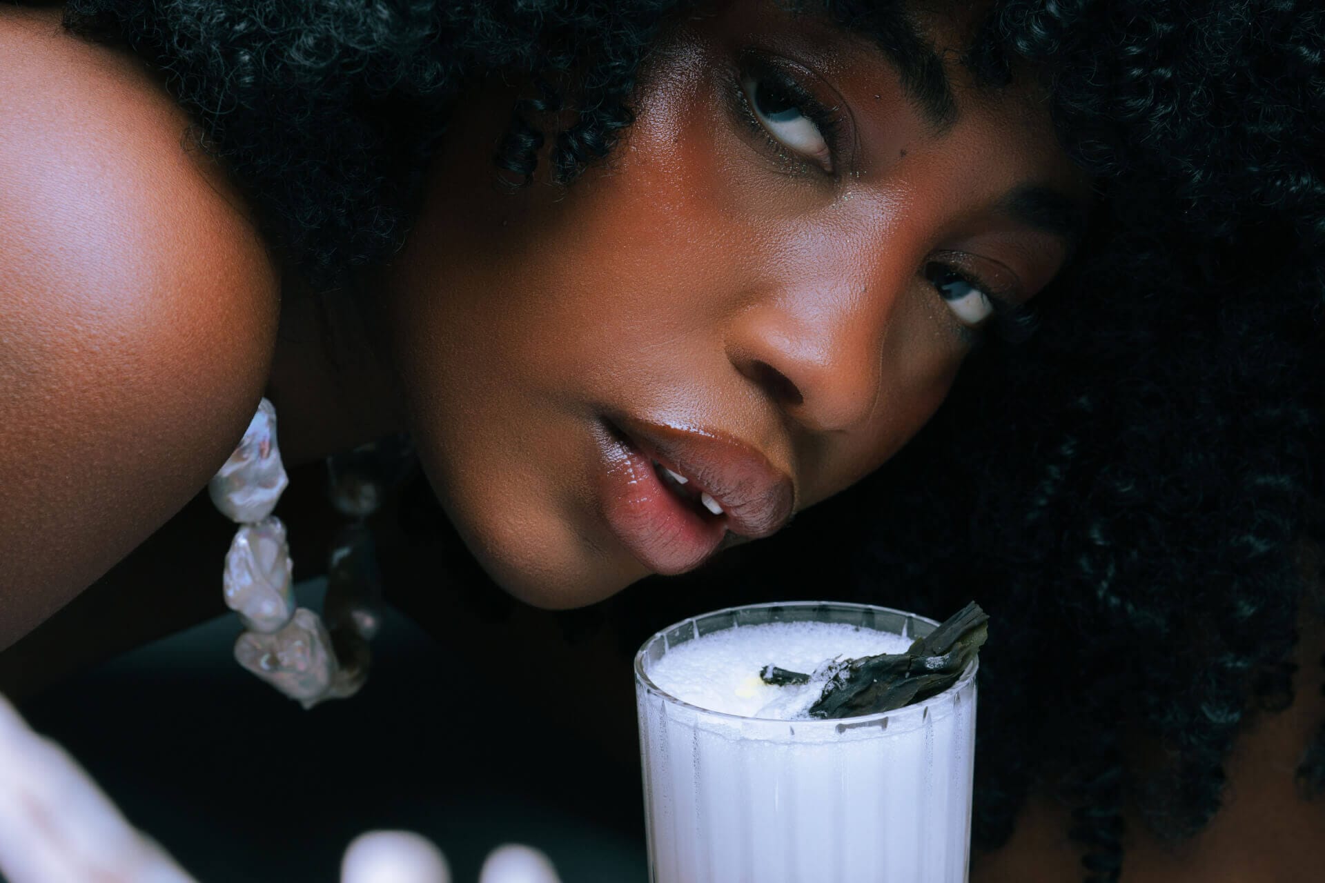 Person with milkshake, wearing curly hair.