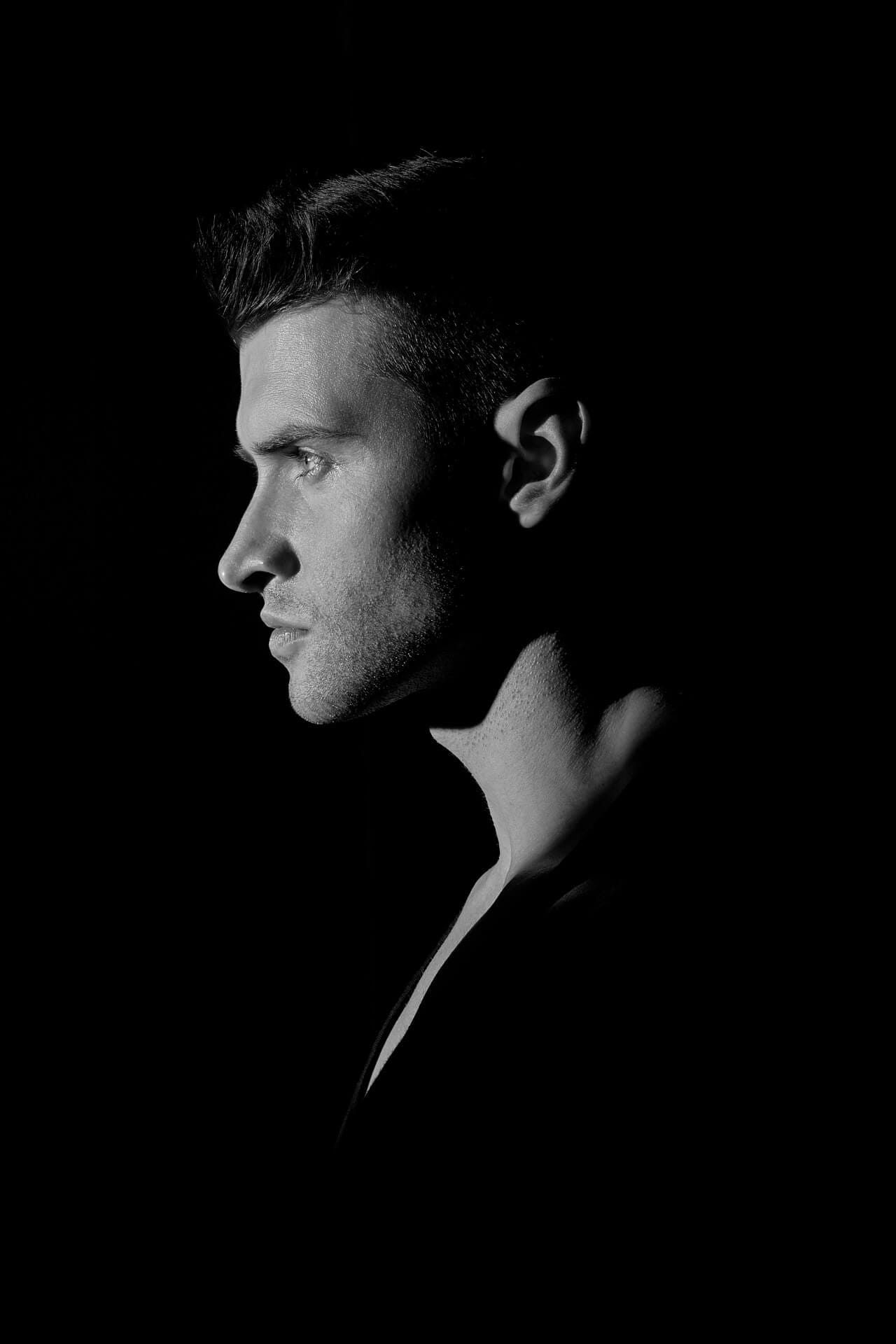 Man in profile, dramatic lighting, black background.
